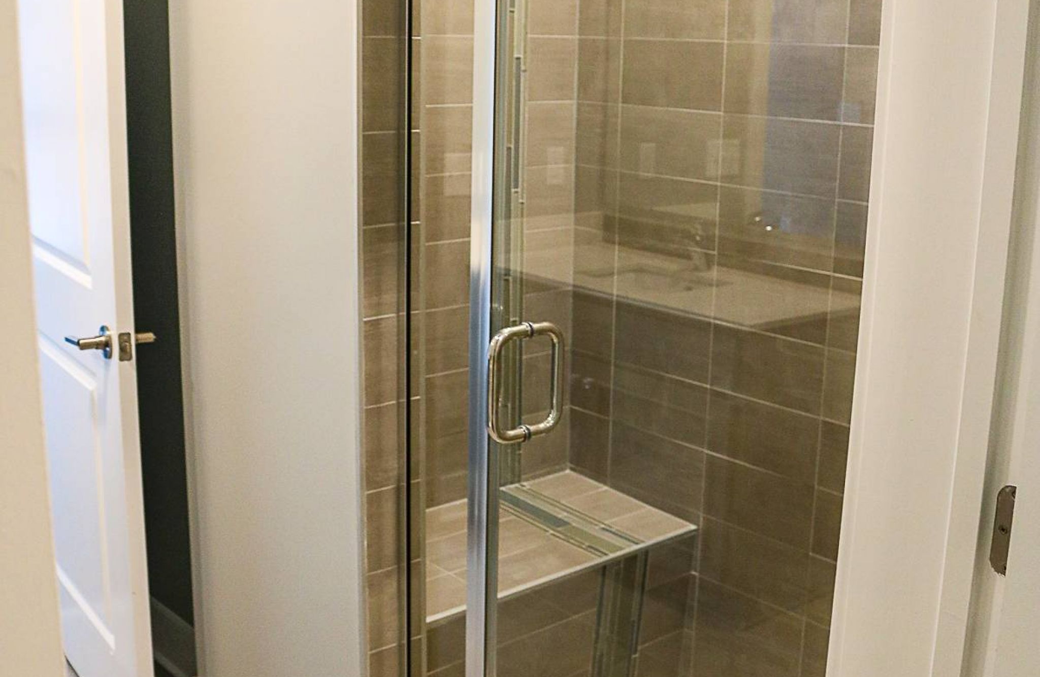Glass shower with beige tiles, built-in bench, and a sliding door in a modern bathroom.