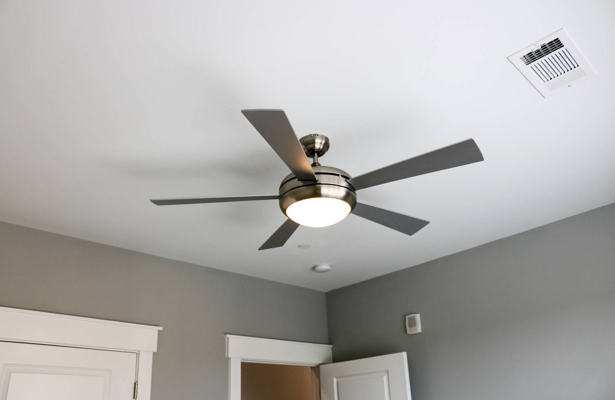 Modern ceiling fan with light fixture spinning in a gray room with white trim and door.