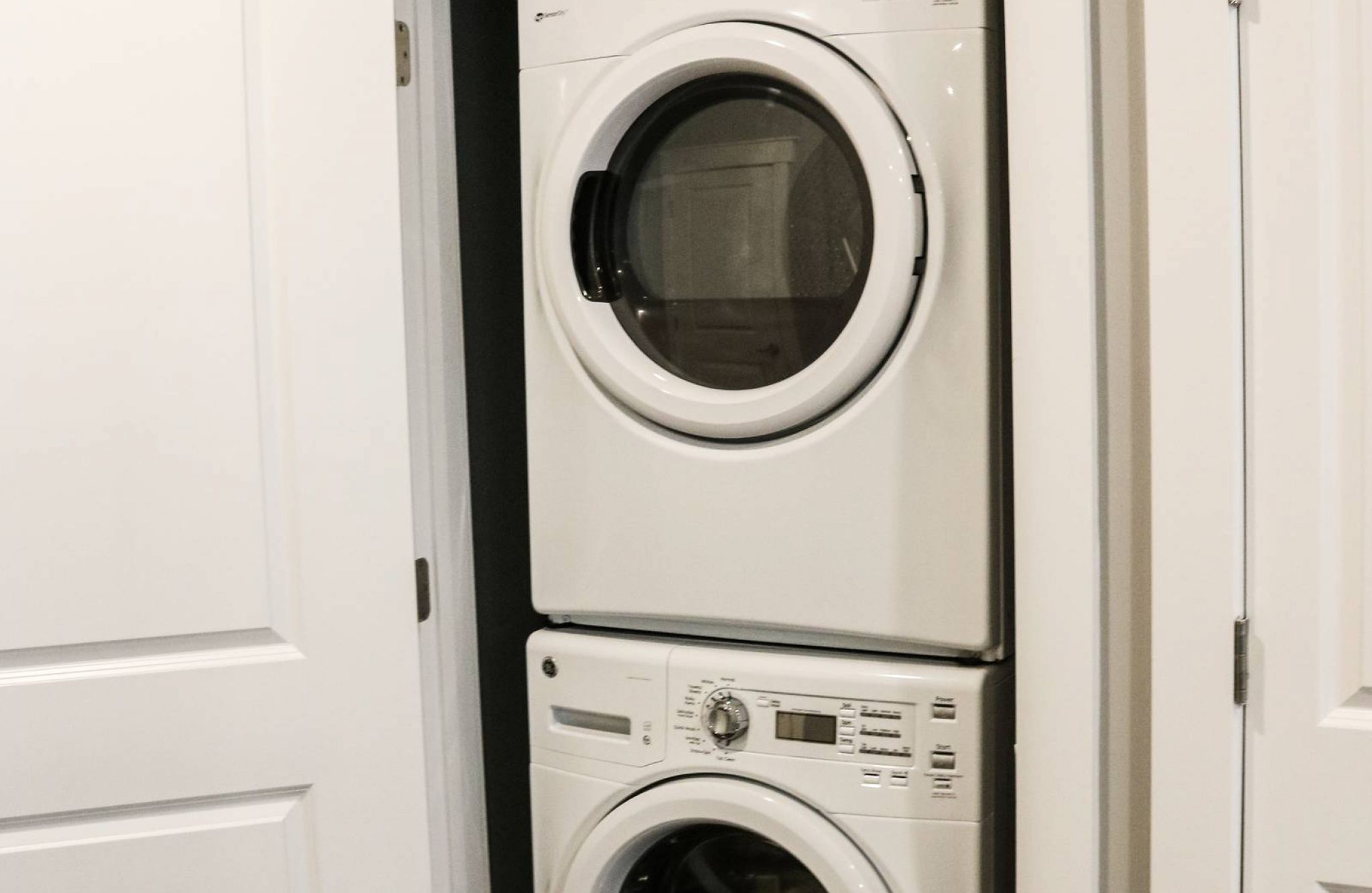 Stacked washer and dryer in a small laundry closet with double white doors open.