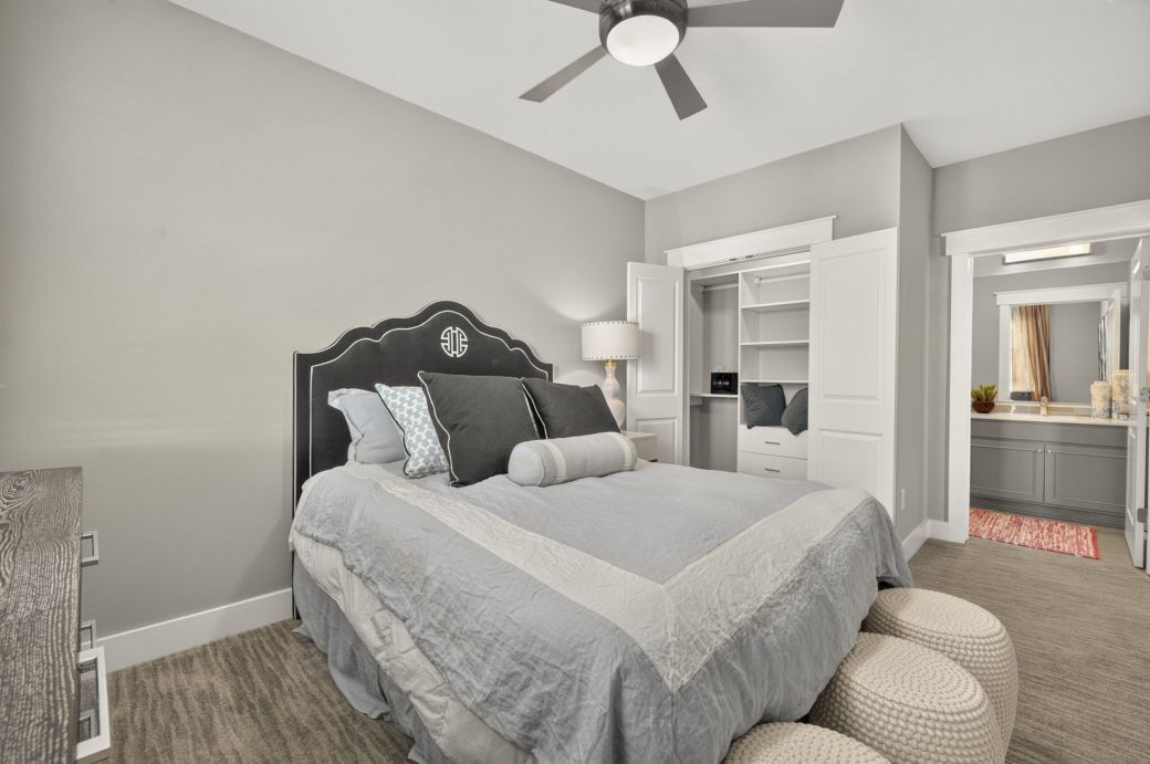 Cozy bedroom with gray bedding, decorative pillows, a black headboard, ottomans at the foot, and an open closet.