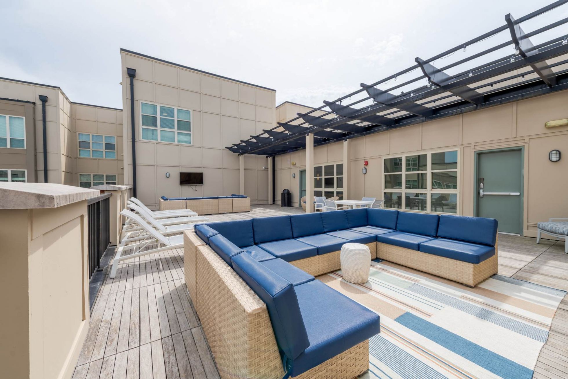Modern rooftop patio with wicker furniture, blue cushions, lounge chairs, and a striped outdoor rug.