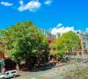 Red brick buildings and trees line a sunny street under a bright blue sky with scattered clouds.