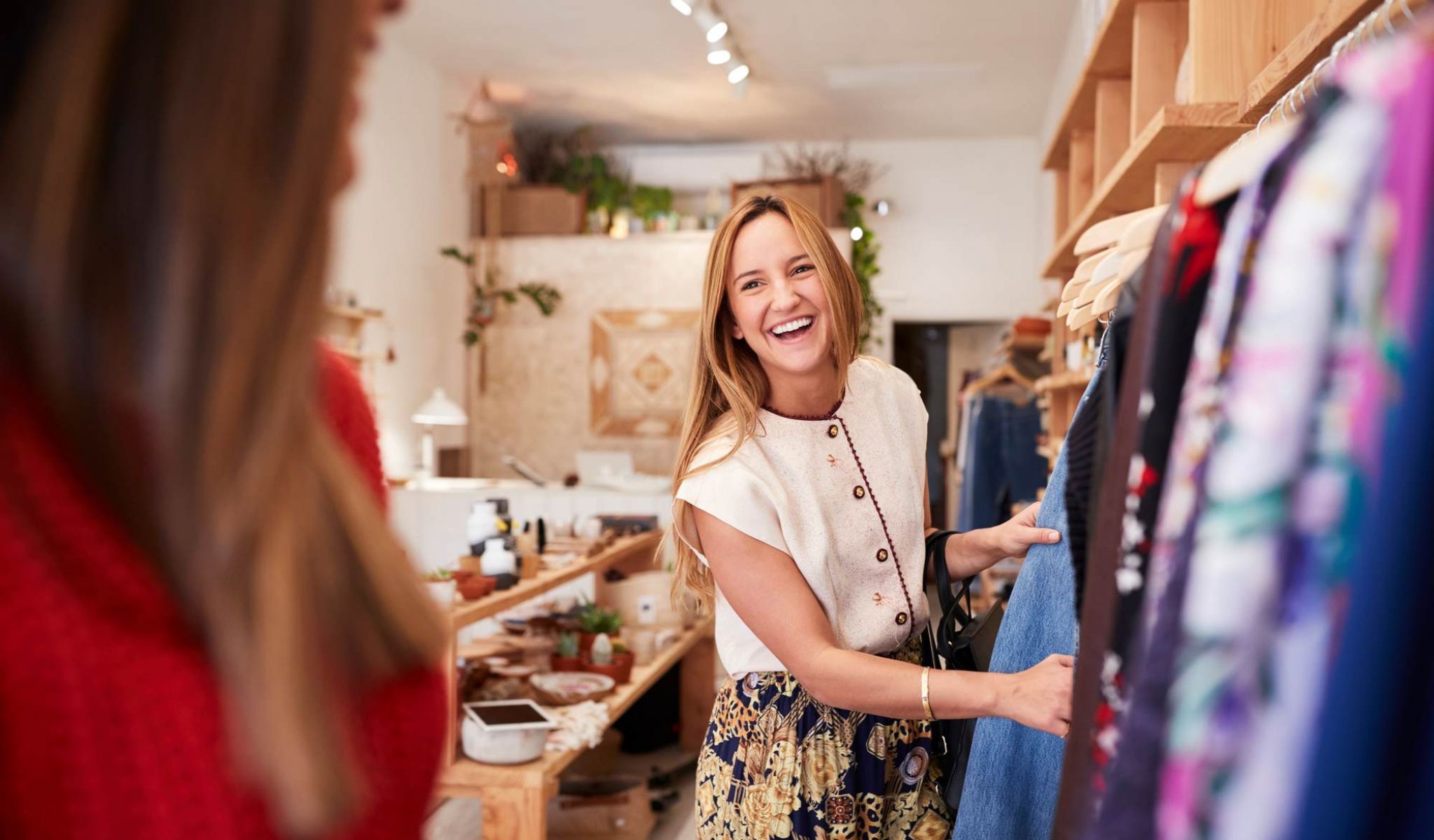 Woman smiling while shopping for clothes in a boutique, standing by a rack of colorful garments.