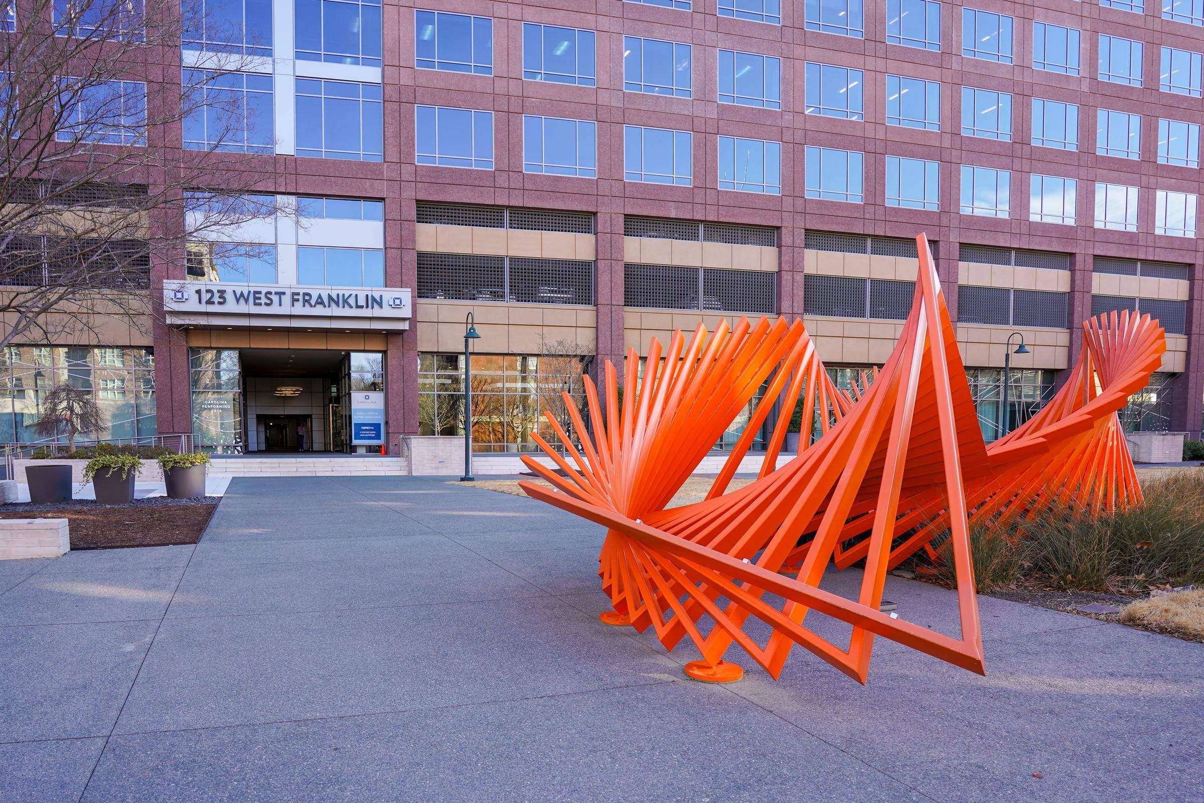 Bright orange abstract metal sculpture in front of a modern office building at 123 West Franklin.