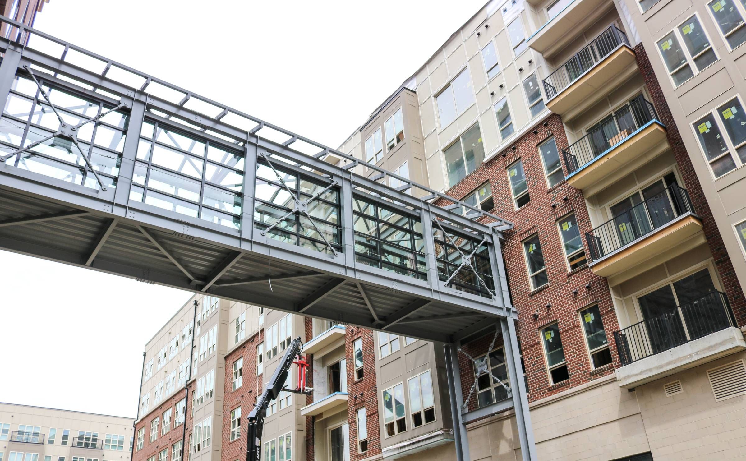 Glass skywalk bridge connects modern apartment buildings with brick and beige exteriors.