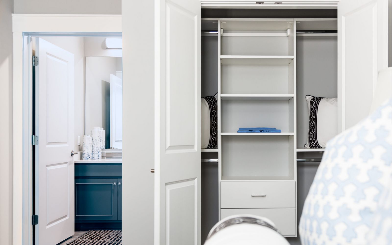 Open closet with shelves and pillows, next to a bathroom with a blue vanity in this stylish 3 Bedroom Apartment at Carolina Square.