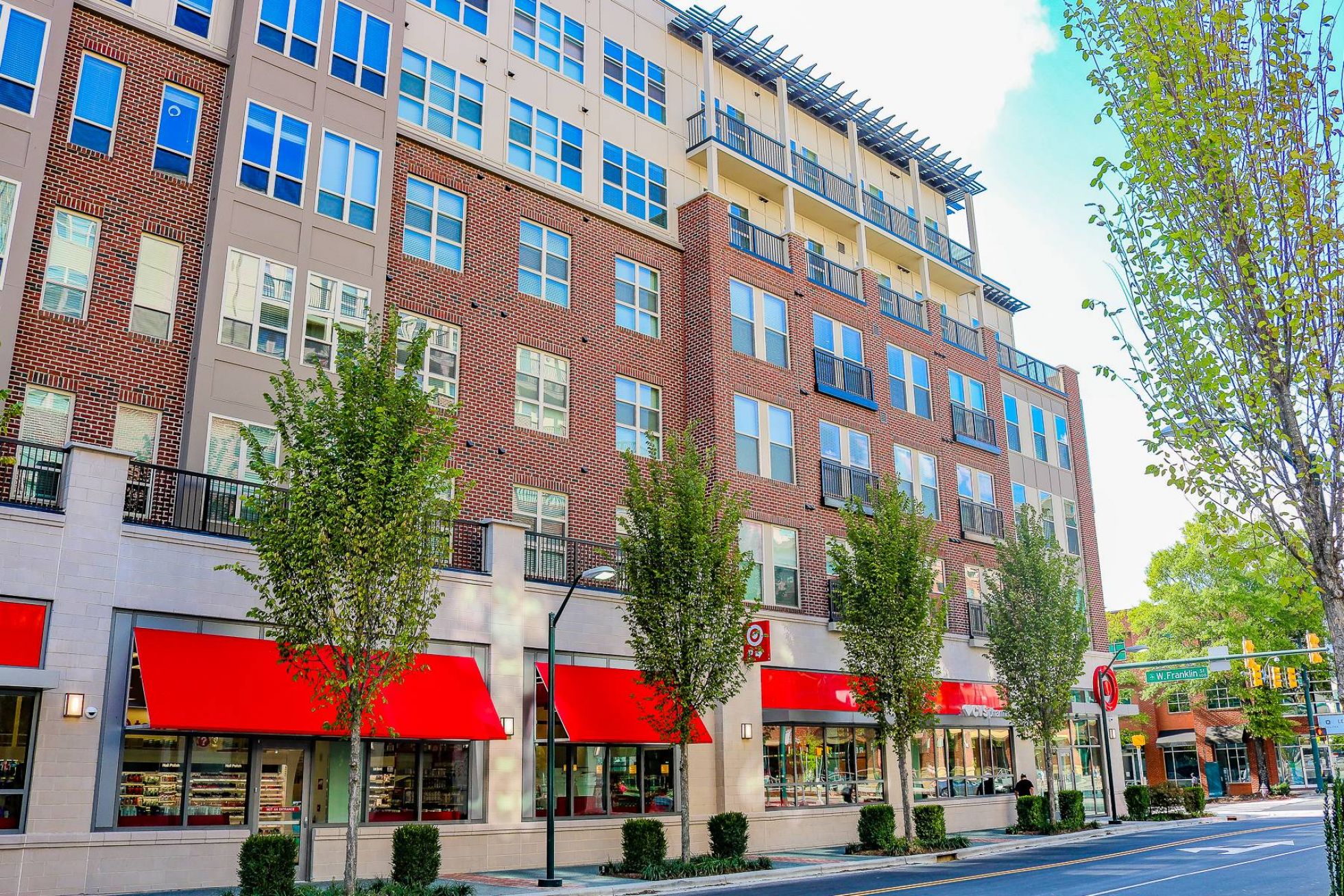 A modern apartment building with red awnings over ground-floor shops and trees lining the sidewalk.