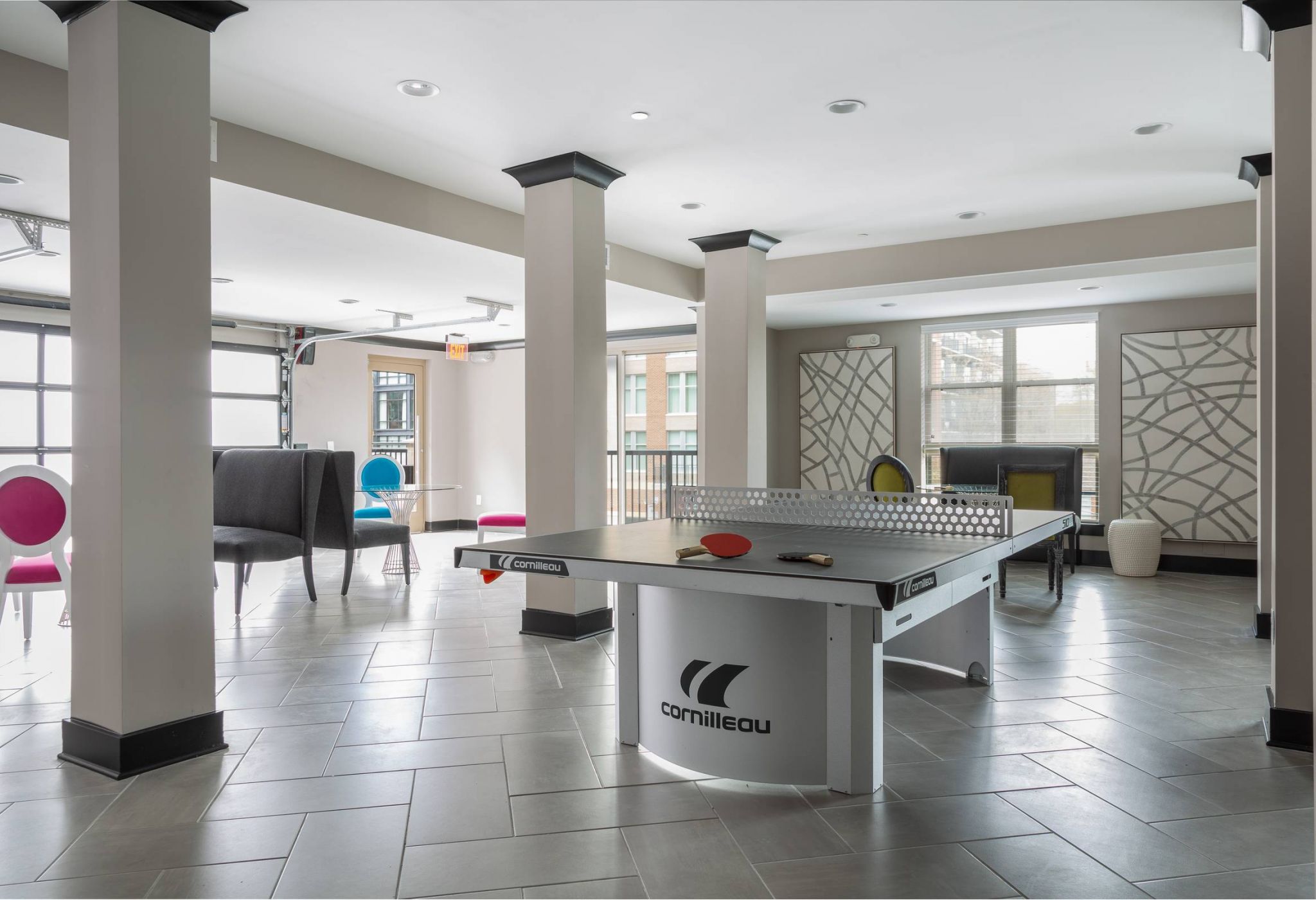 Modern room with a Cornilleau ping pong table, colorful chairs, and large windows letting in natural light.