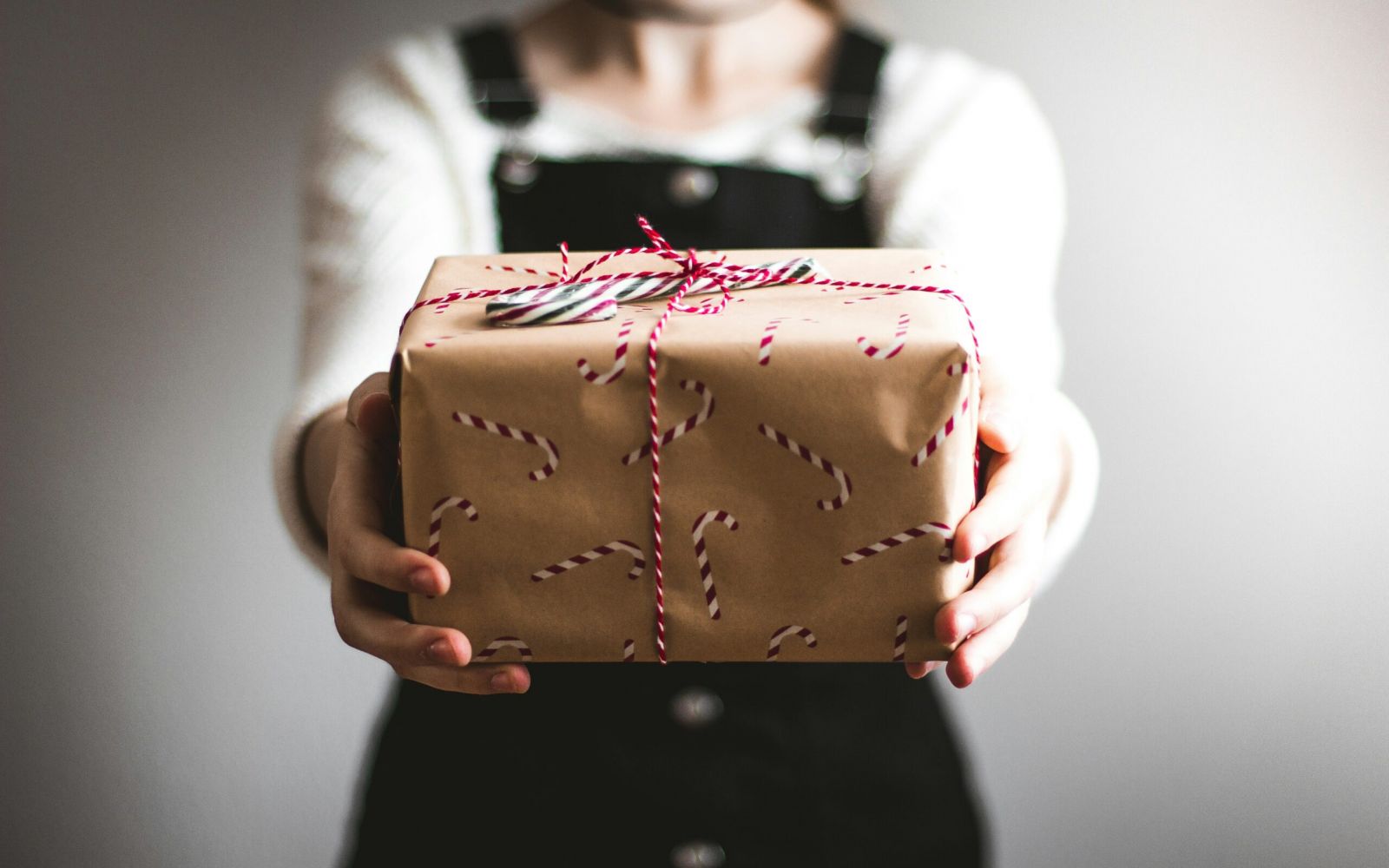 Person holding out a gift wrapped in candy cane-patterned paper and tied with red and white string.