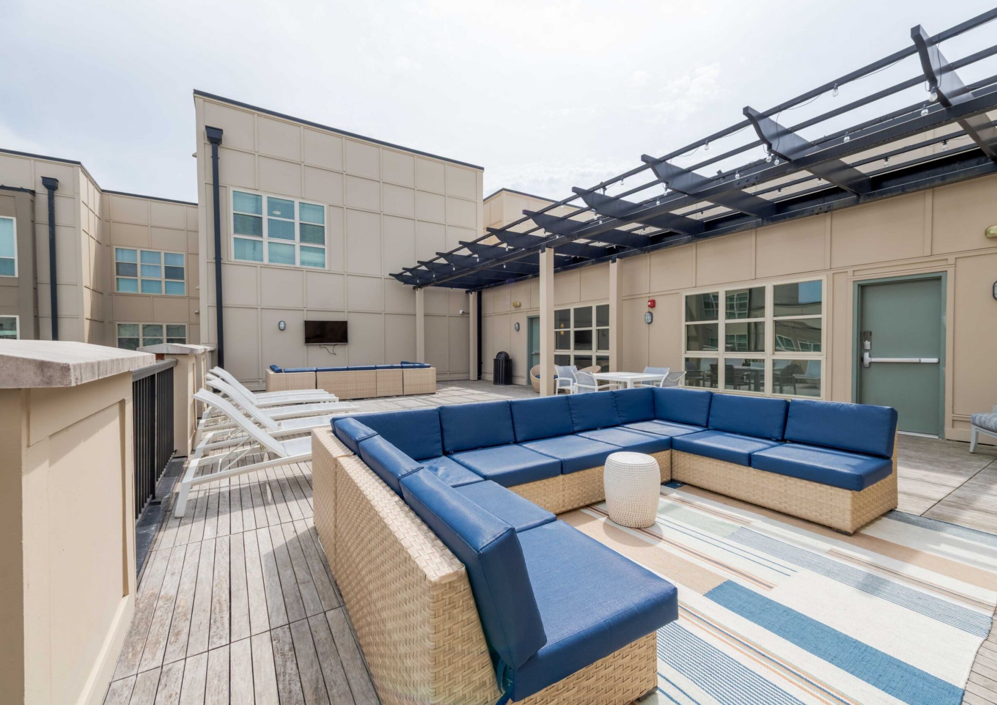 Outdoor rooftop patio with blue cushioned seating, lounge chairs, and a rug on wooden flooring.