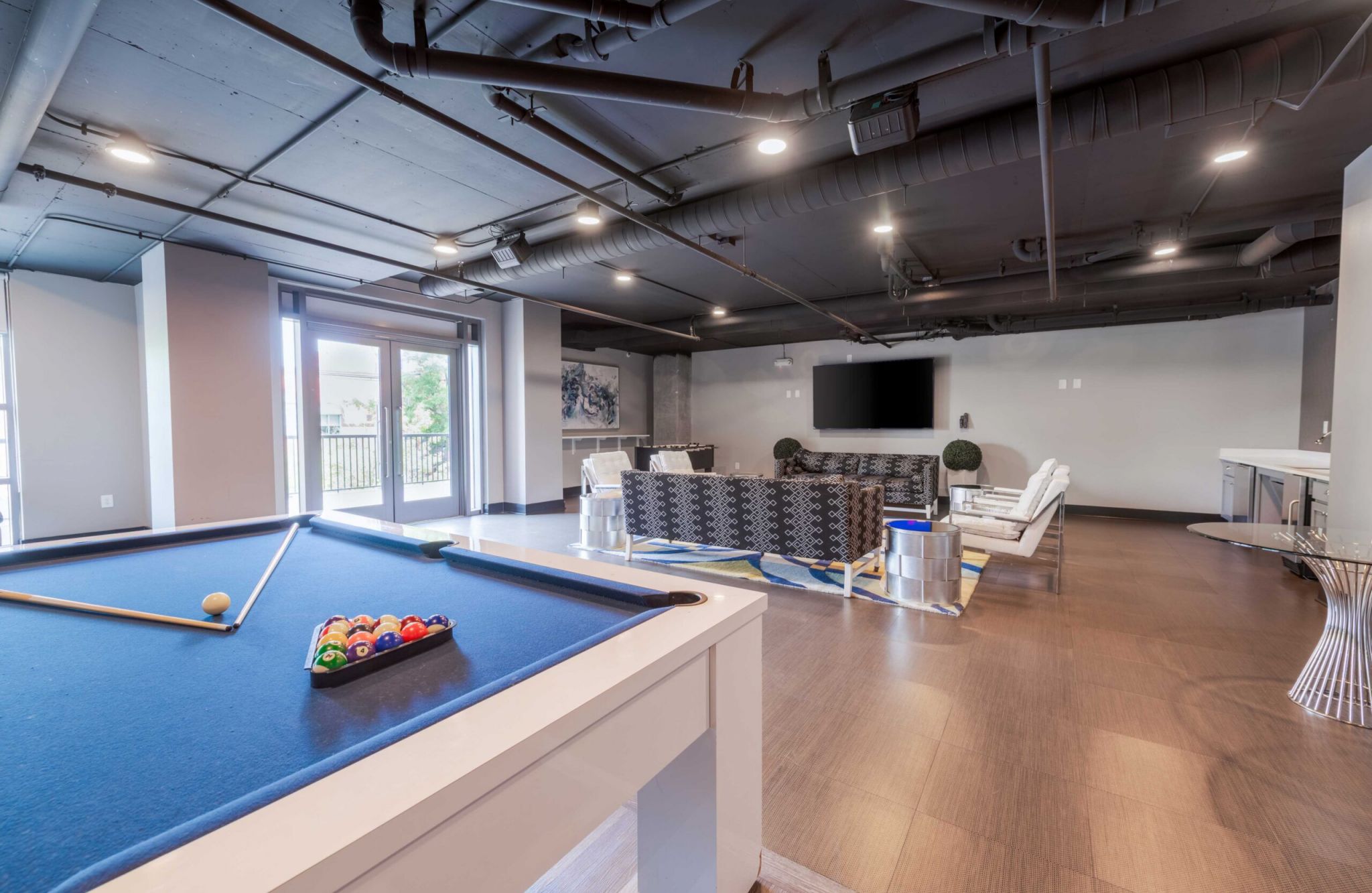 Modern lounge with a blue pool table, seating area, large TV, and wood flooring.