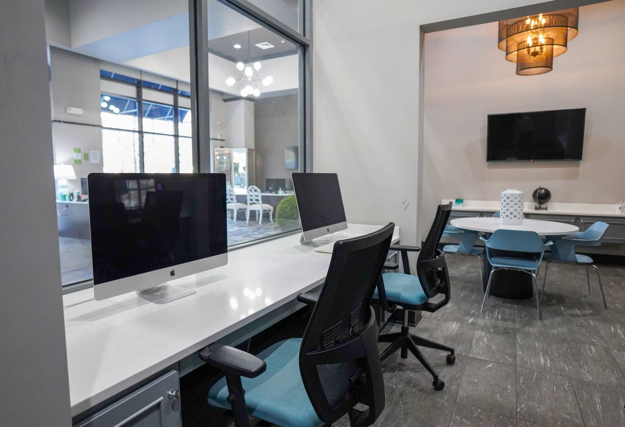 Modern office space with computers on desks, chairs, and a TV mounted on the wall in the background.