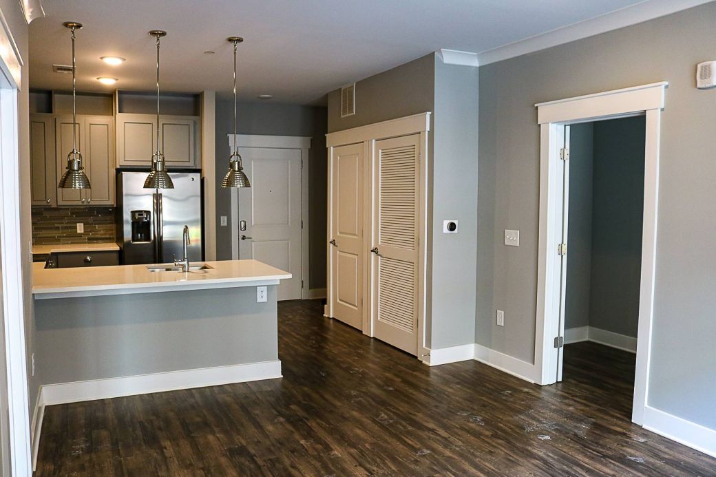 Modern apartment interior with gray walls, hardwood floors, open kitchen, and pendant lights over a white island at Carolina Square apartments.