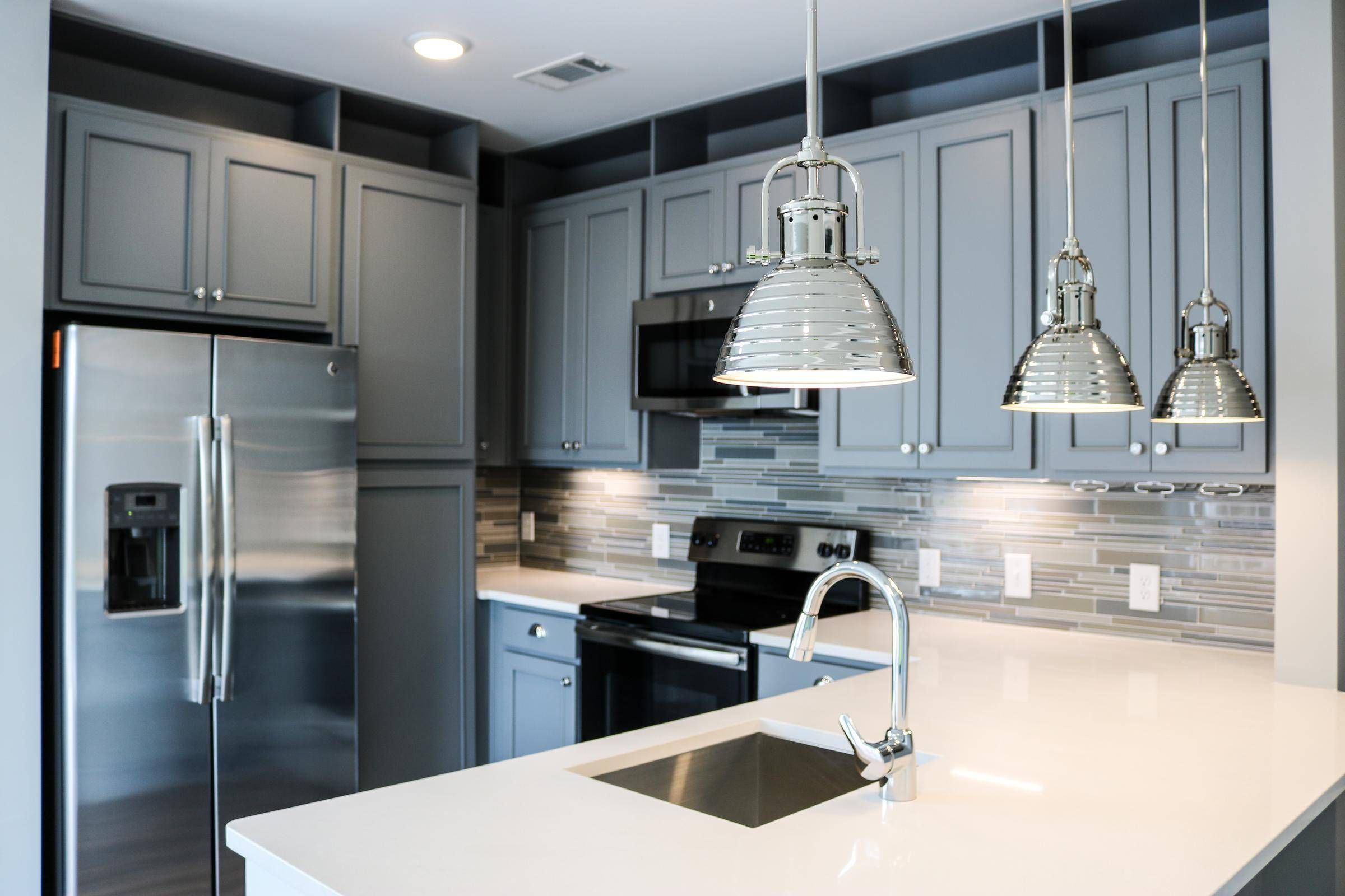 Modern kitchen with gray cabinets, stainless steel appliances, pendant lights, and a white island sink at Carolina Square apartments
