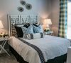 Modern bedroom with geometric headboard, patterned pillows, bedside lamps, flowers, and plaid curtains at Carolina Square apartments.