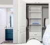Open closet with white shelves and pillows, next to a bathroom with a blue vanity and open door.