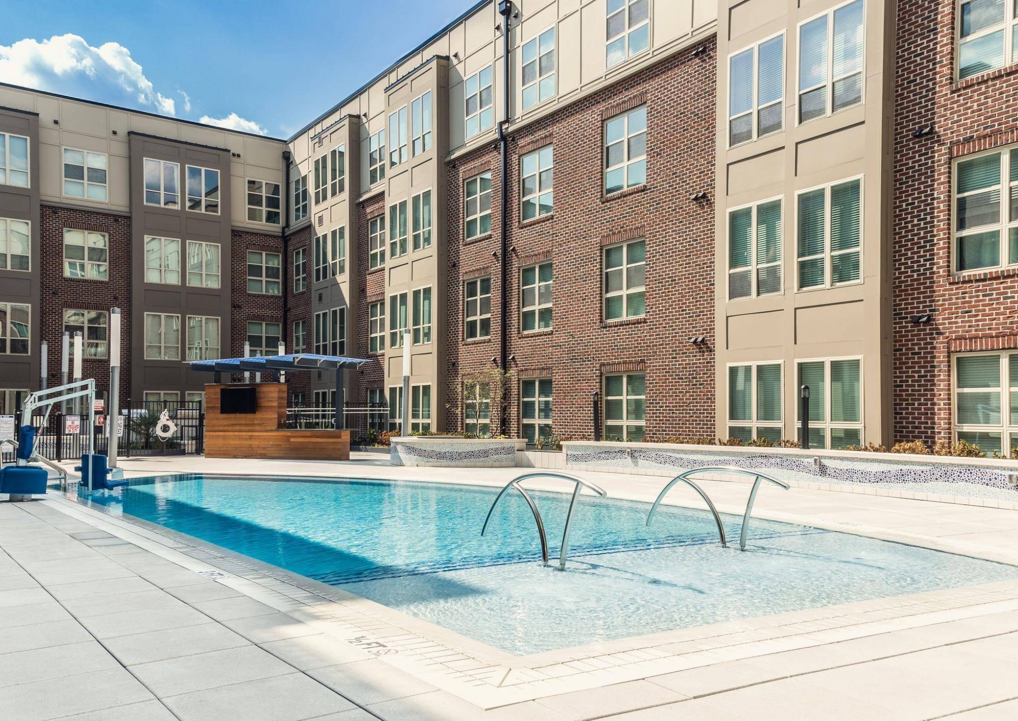 Outdoor pool surrounded by modern brick apartment buildings with large windows and a shaded seating area.