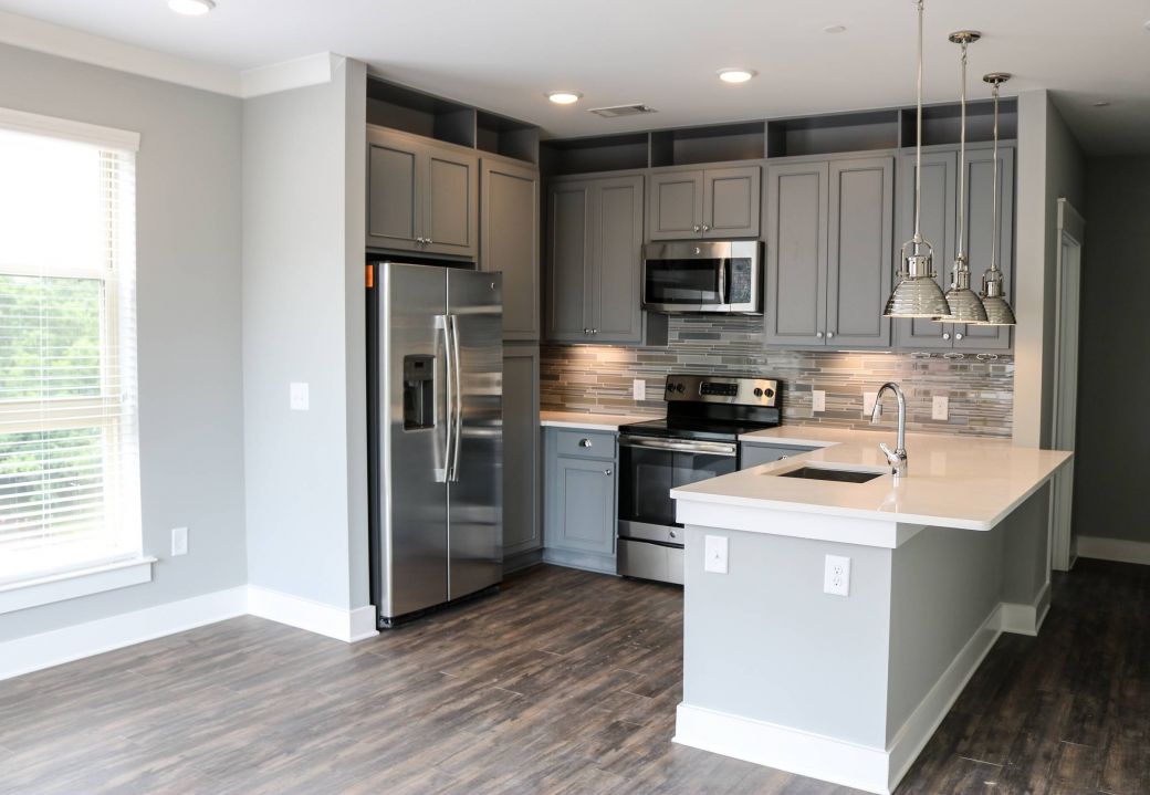 Modern kitchen with gray cabinets, stainless steel appliances, island, and pendant lights over wood flooring at Carolina Square apartments.
