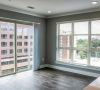 Modern apartment room with large windows, blinds, and wood floors, overlooking city buildings and greenery at Carolina Square apartments