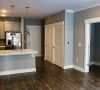 Modern apartment interior with gray walls, hardwood floors, open kitchen, and pendant lights over a white island at Carolina Square apartments.