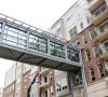 Glass skywalk bridge connects modern apartment buildings with brick and beige exteriors.