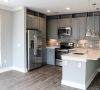 Modern kitchen with gray cabinets, stainless steel appliances, island, and pendant lights over wood flooring at Carolina Square apartments.