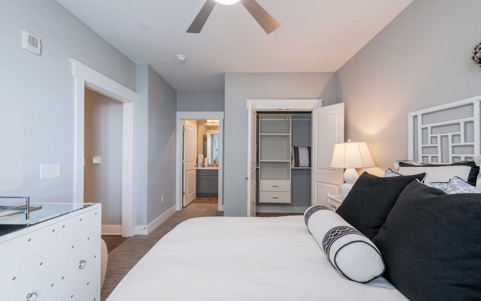 Modern bedroom at Carolina Square with a neat bed, open closet, dresser, and view into a bathroom near UNC Chapel Hill.
