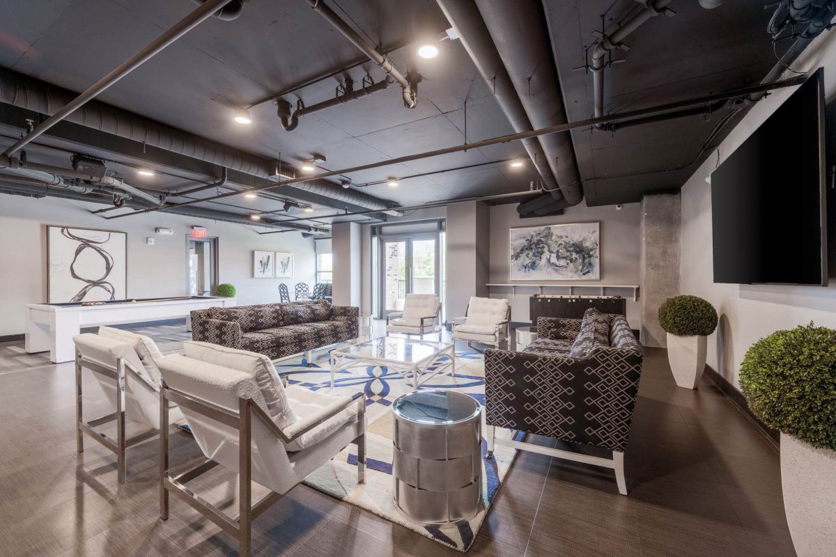 Modern lounge with patterned chairs, white armchairs, artwork, a pool table, and large windows.