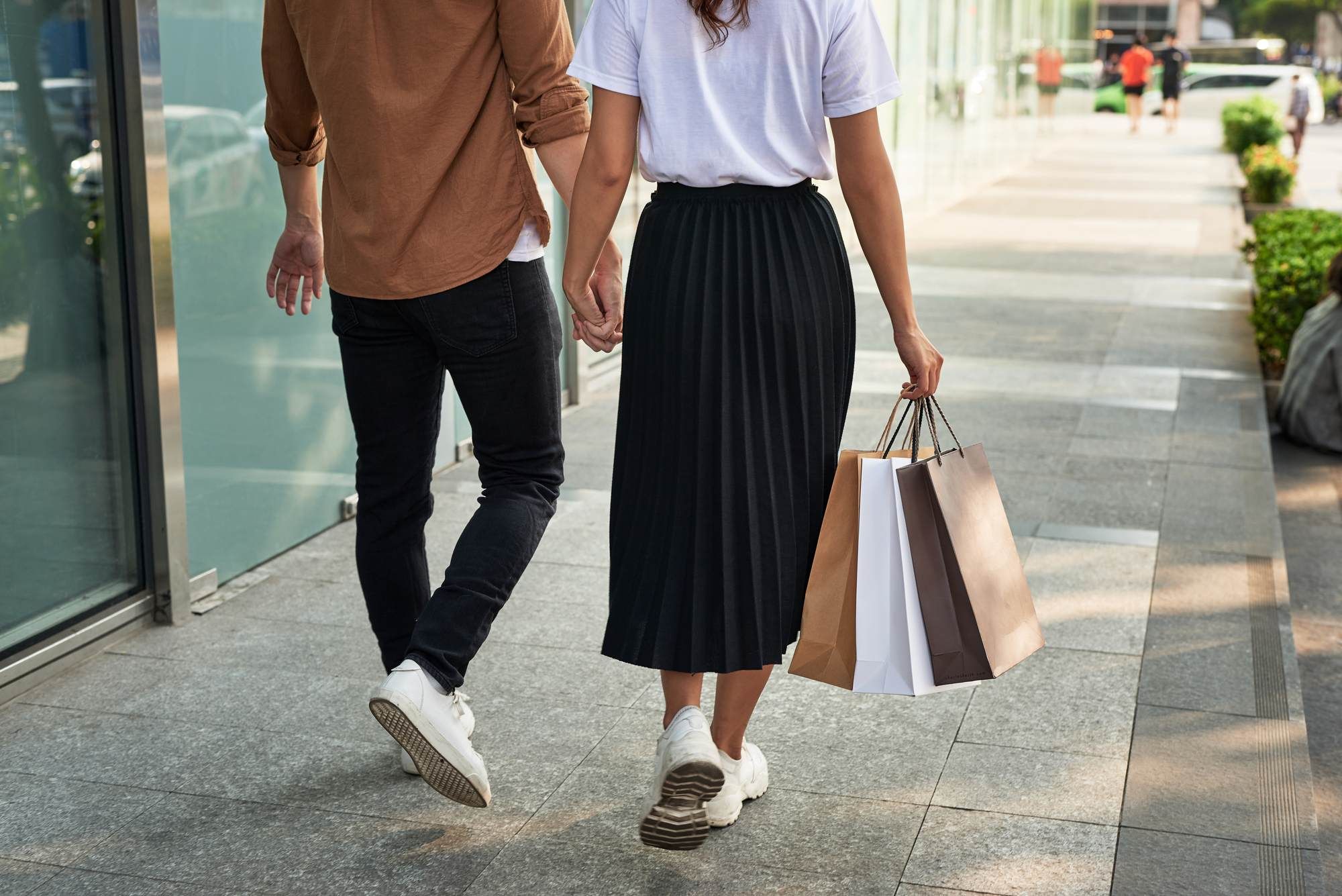 A couple holding hands and carrying shopping bags while walking on a city sidewalk.