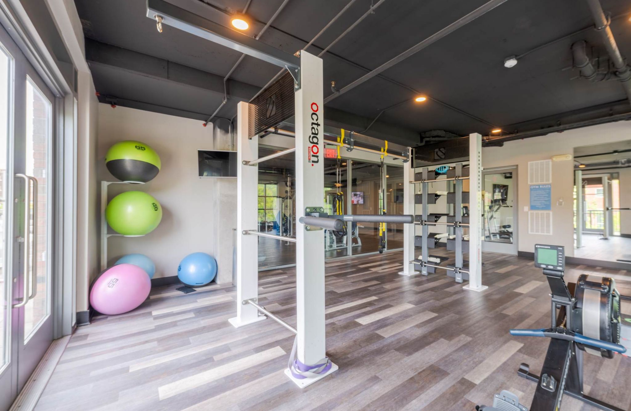 Modern gym with exercise balls, weight racks, workout machines, and large windows letting in natural light.