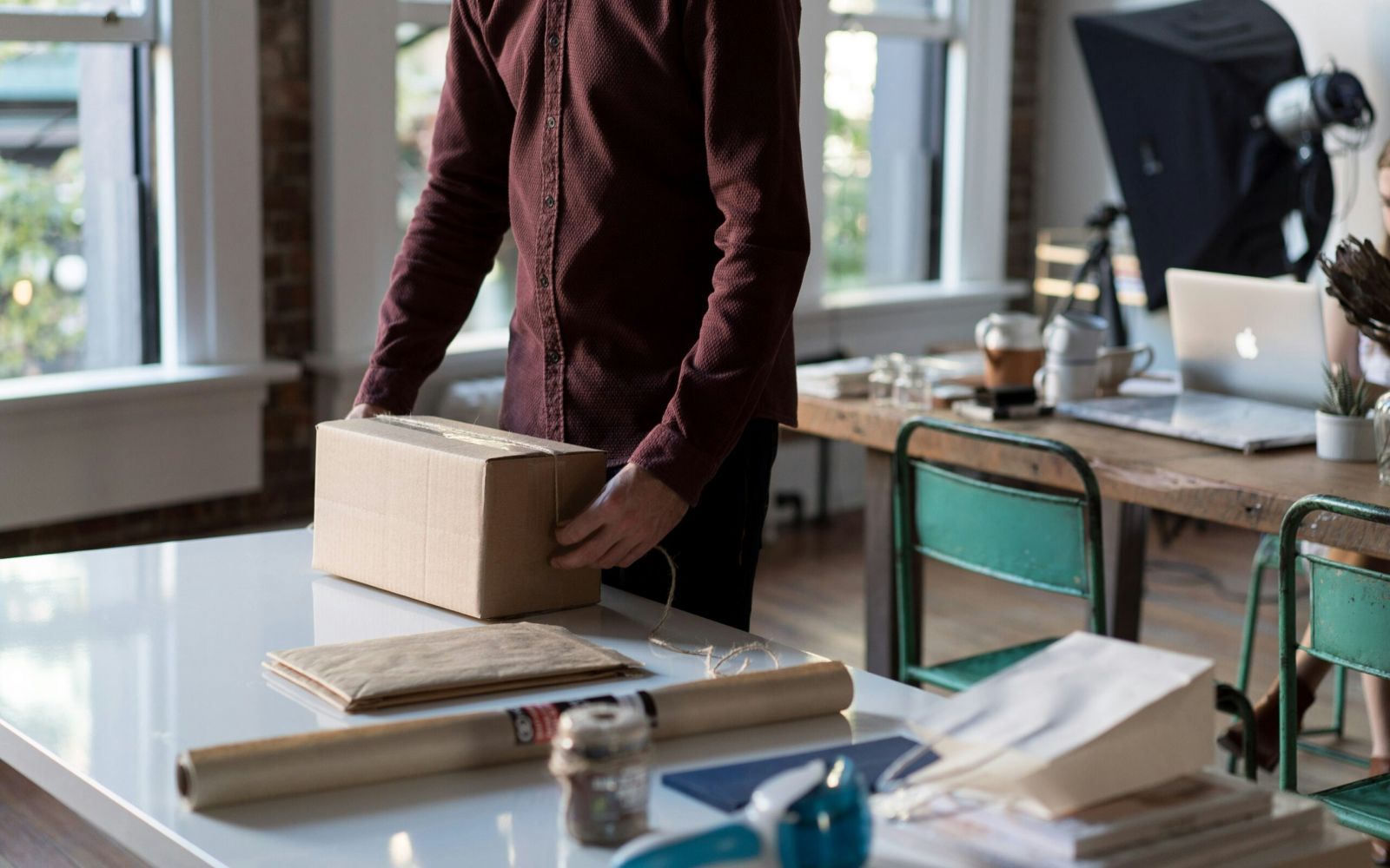 Person in a maroon shirt packing a cardboard box on a white desk with office supplies nearby.