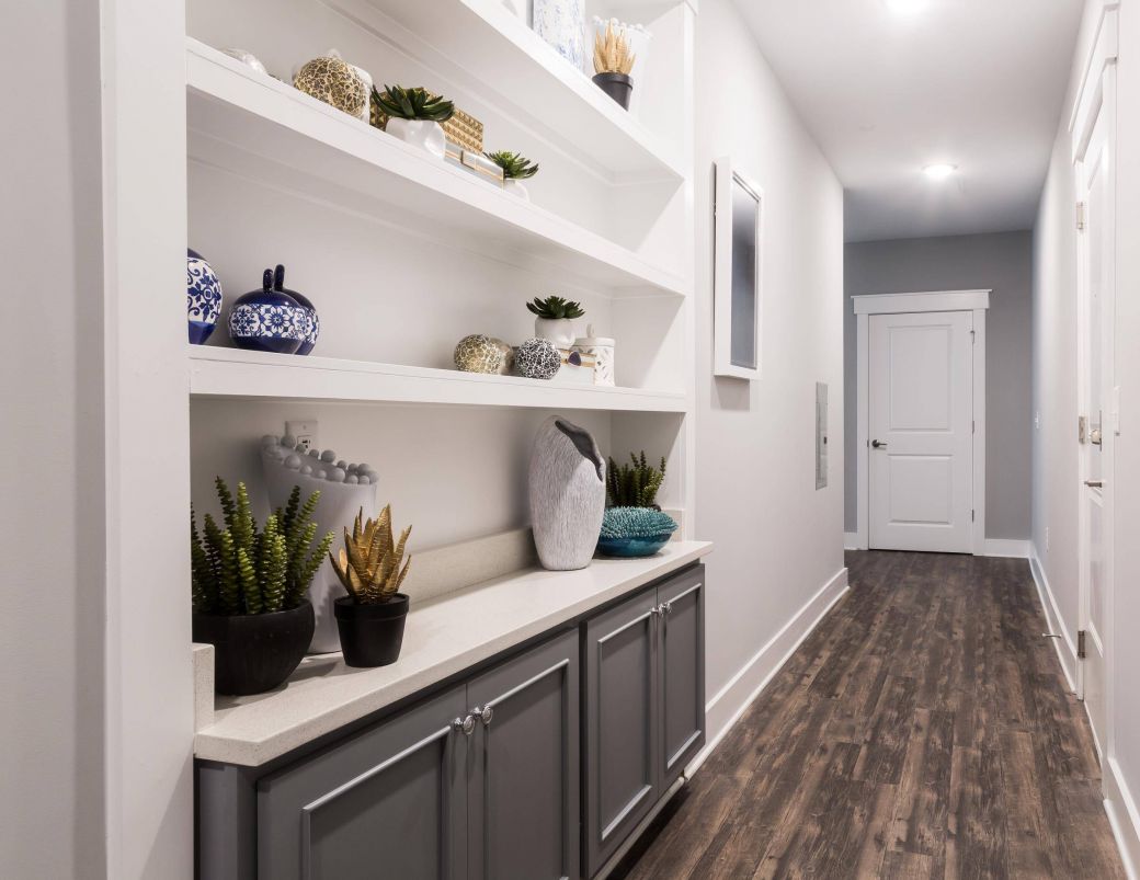 Modern hallway with wooden floors, white shelves, potted plants, and decorative vases on built-in cabinetry at Carolina Square apartments