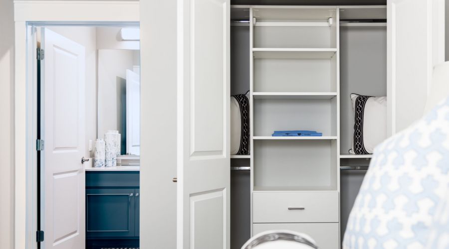 Open closet with shelves and pillows, next to a bathroom with a blue vanity in this stylish 3 Bedroom Apartment at Carolina Square.