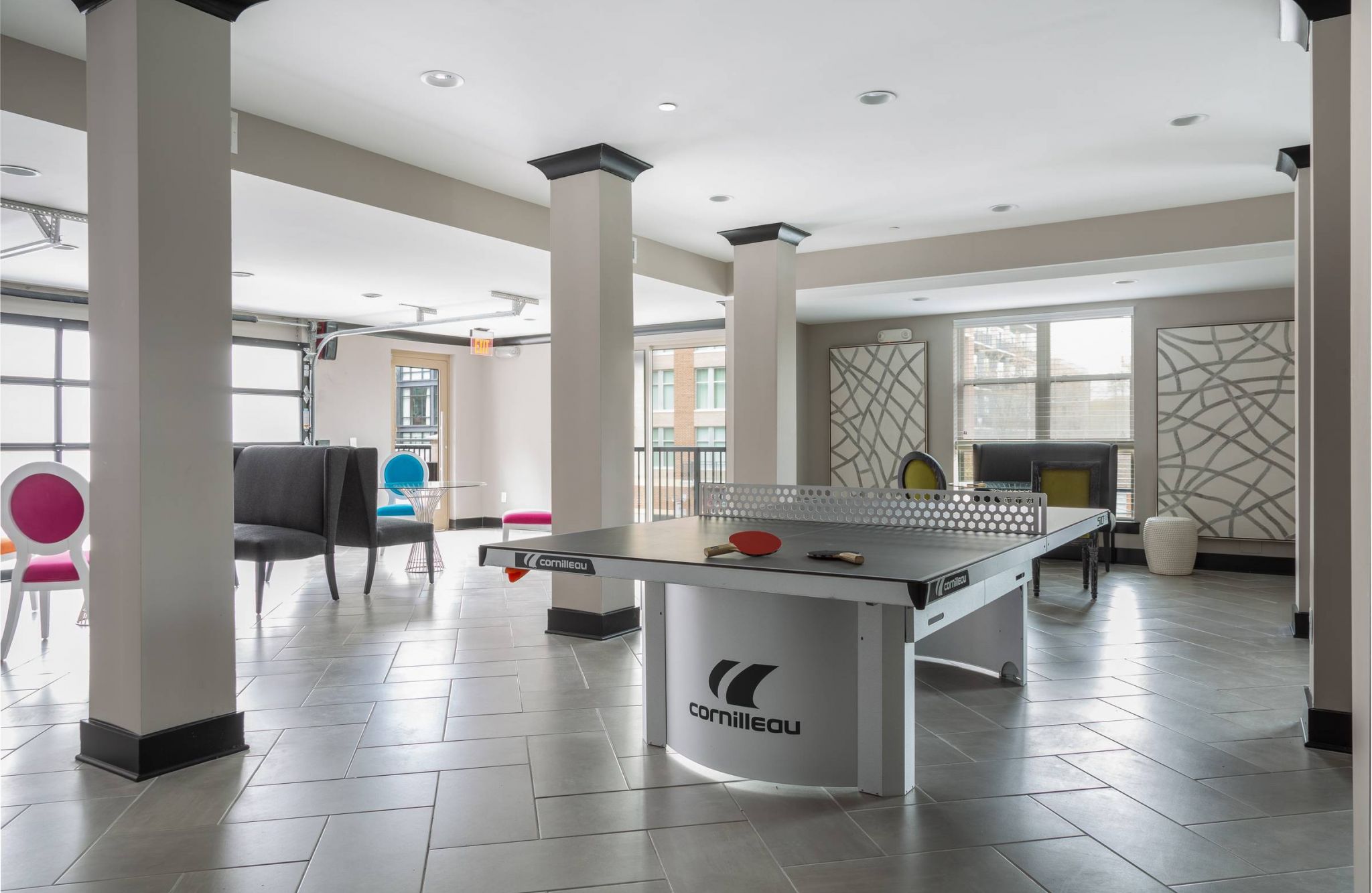 Modern room with a Cornilleau ping pong table, colorful chairs, and large windows letting in natural light.