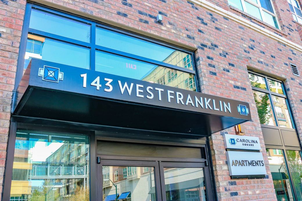 Modern brick apartment building entrance with a sign reading “143 West Franklin” above glass doors.