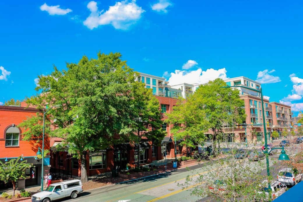 Red brick buildings and trees line a sunny street under a bright blue sky with scattered clouds.