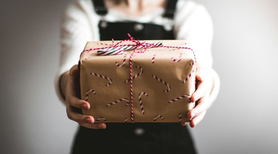 Person holding out a gift wrapped in candy cane-patterned paper and tied with red and white string.