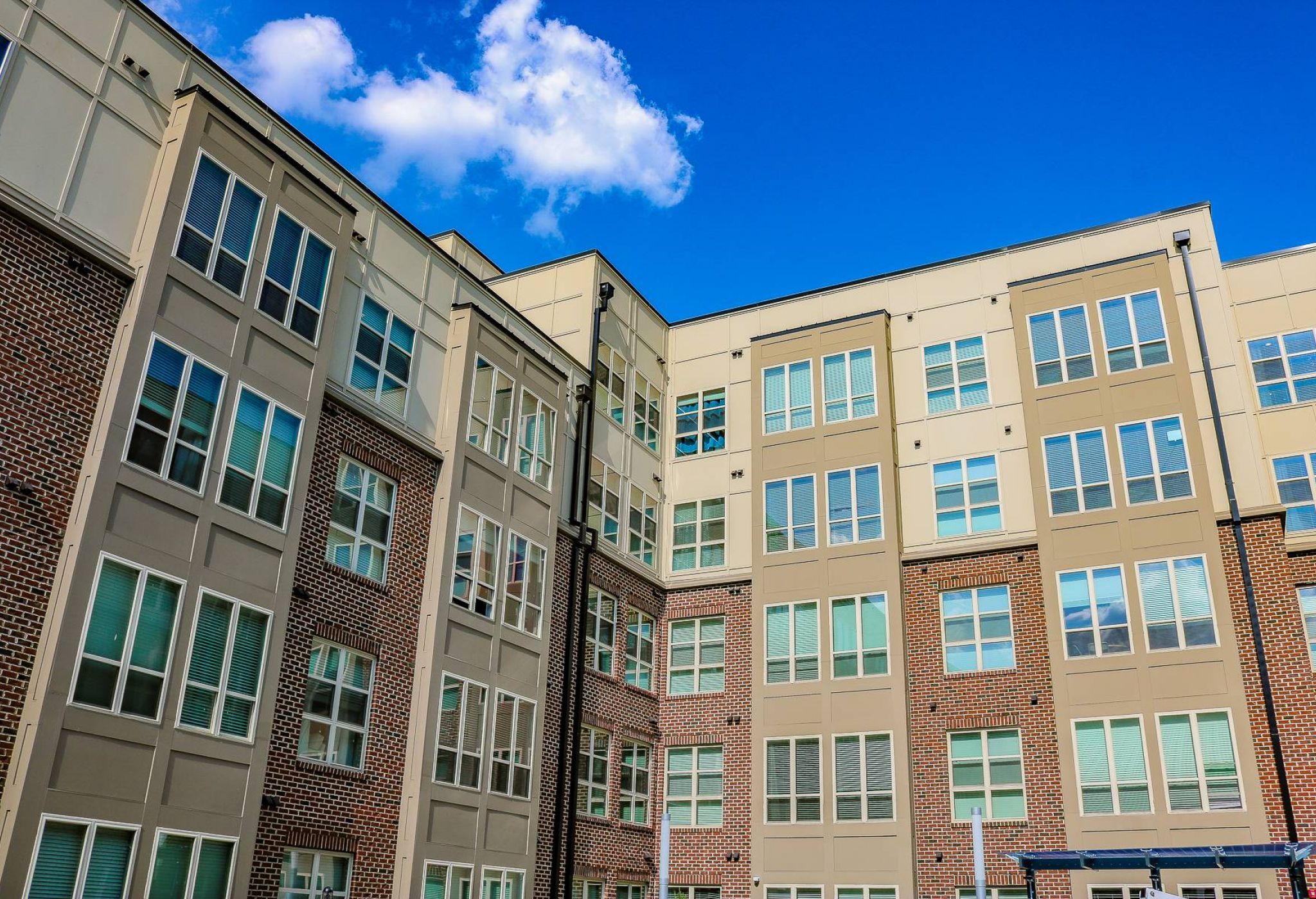 Modern apartment building with large windows against a bright blue sky with a few clouds.