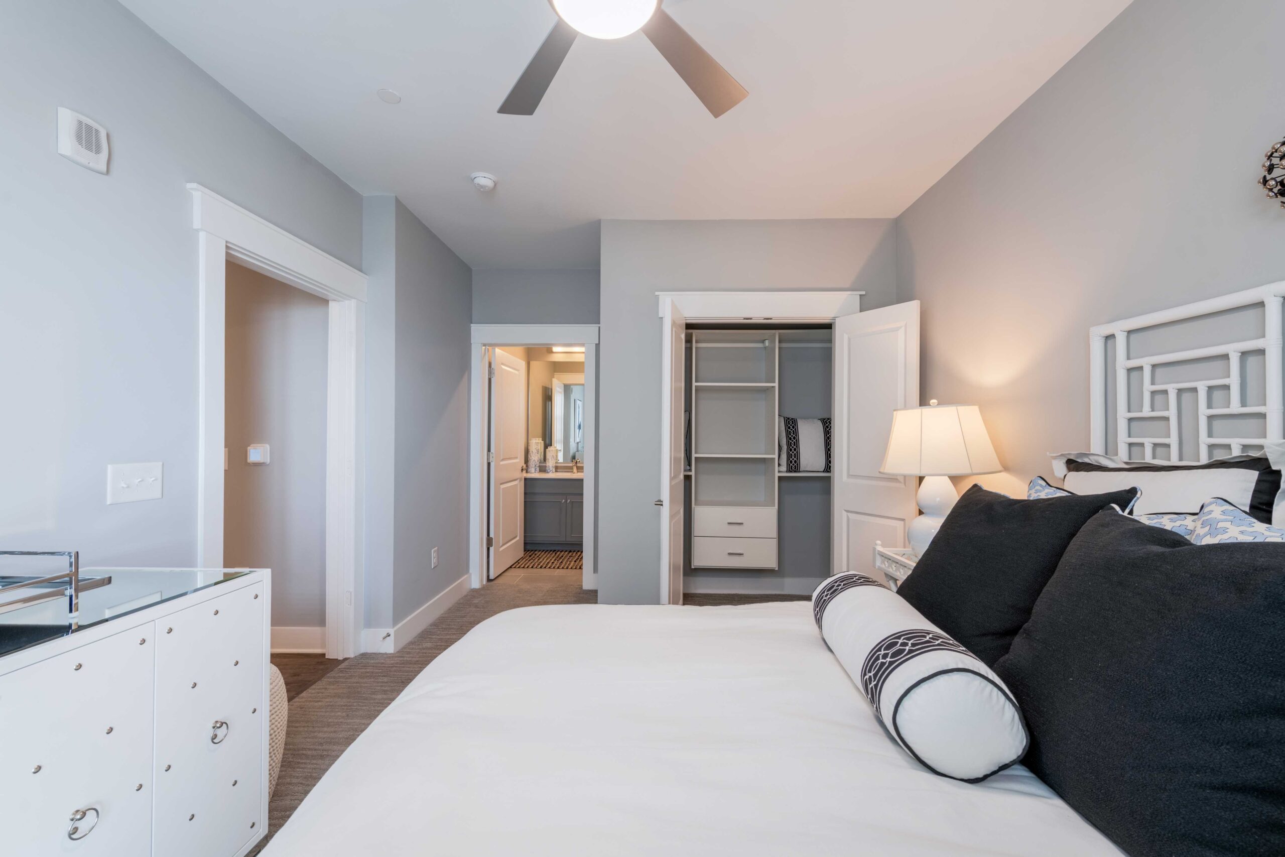 Modern bedroom at Carolina Square with a neat bed, open closet, dresser, and view into a bathroom near UNC Chapel Hill.