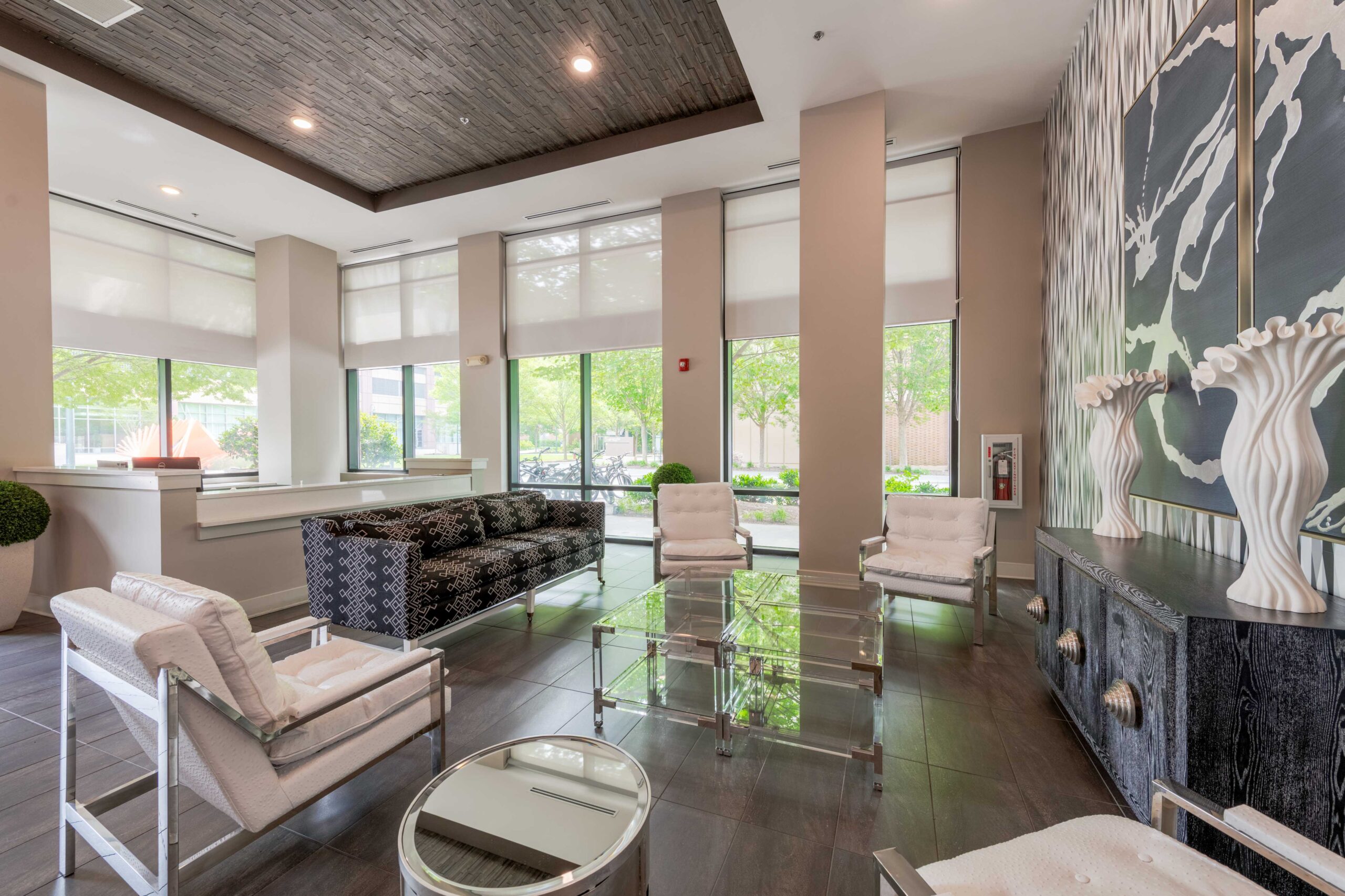 Modern lobby with large windows, stylish seating, glass tables, and decorative wall art and sculptures.