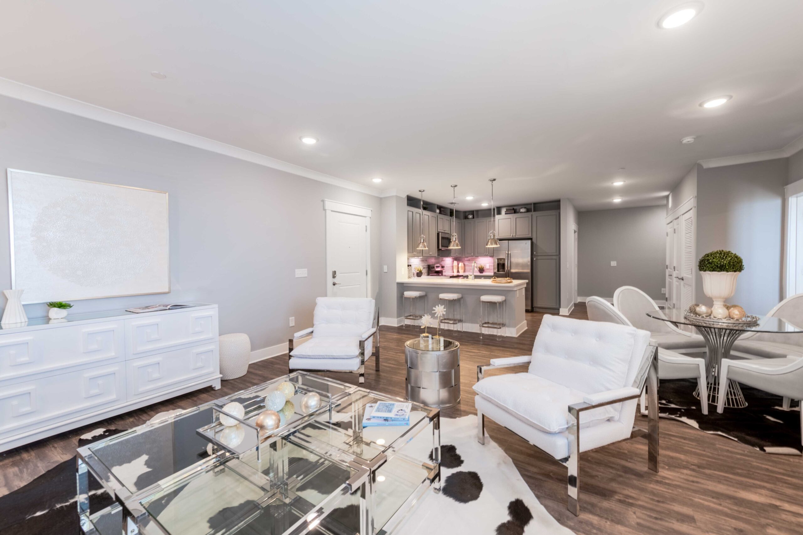 Modern open-concept living room and kitchen with white furniture and stainless steel appliances.