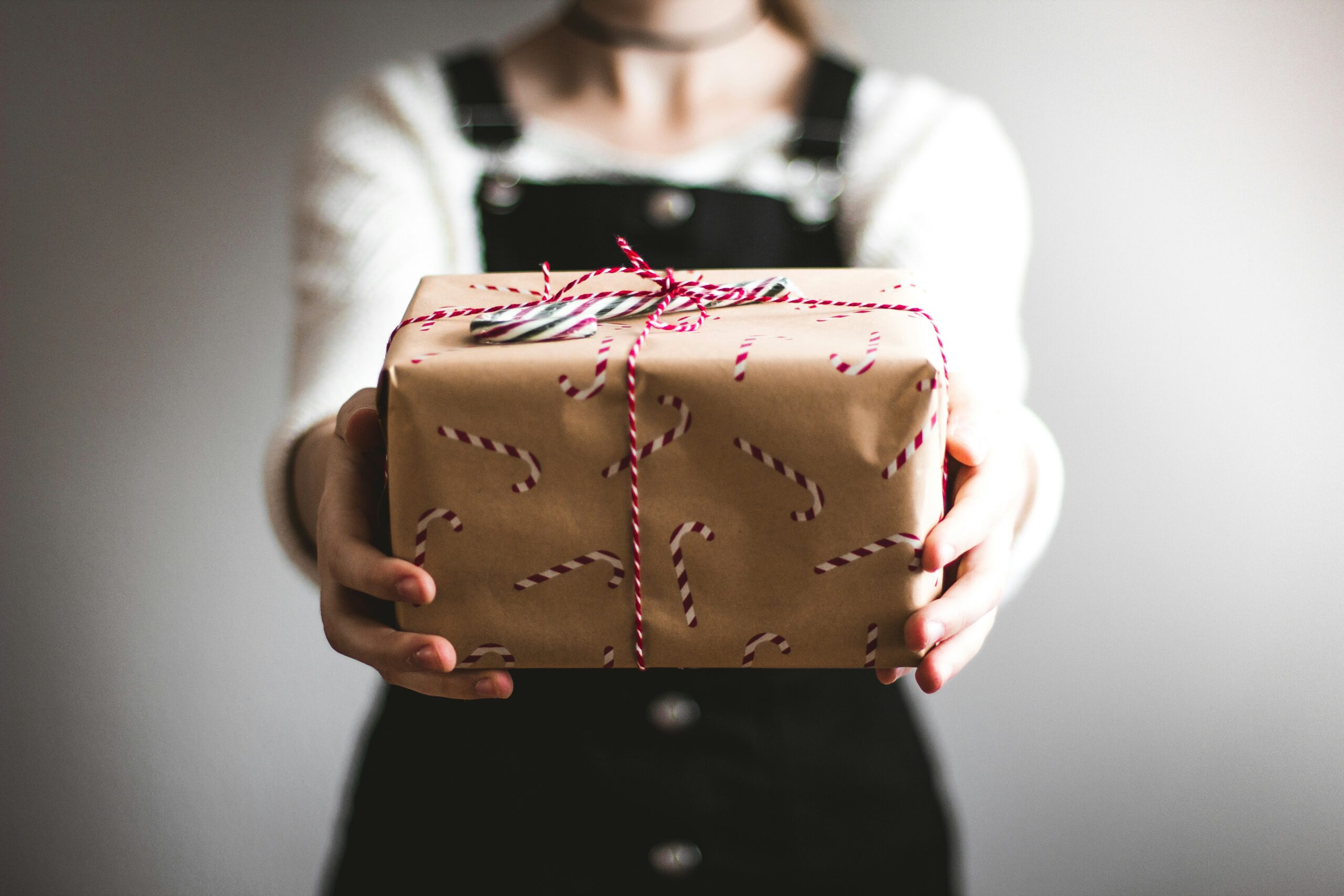 Person holding out a gift wrapped in candy cane-patterned paper and tied with red and white string.