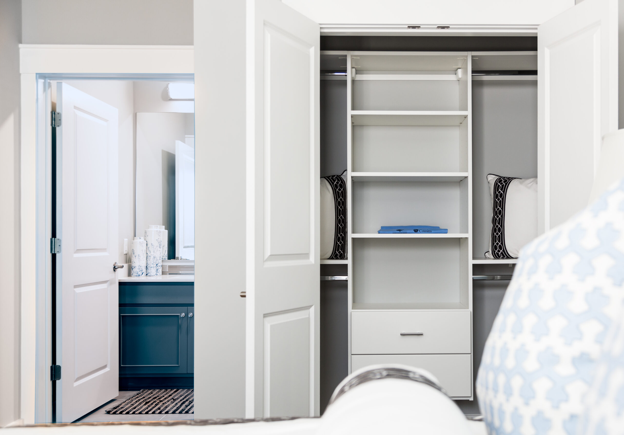 Open closet with shelves and pillows, next to a bathroom with a blue vanity in this stylish 3 Bedroom Apartment at Carolina Square.