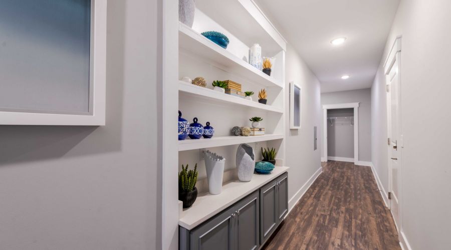 A hallway with wooden floors, built-in shelves holding decor, and an open closet at the end.
