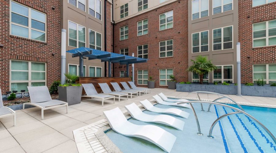 Modern apartment courtyard at Carolina Square with pool, lounge chairs, and shaded seating—ideal for UNC sophomores seeking on-campus housing.