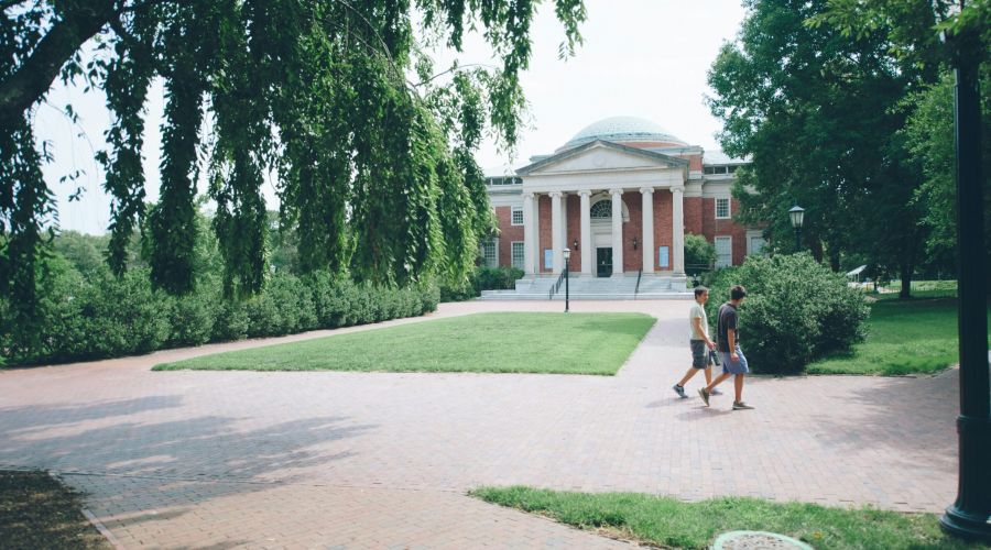 Two people walk on a brick path in front of a large, domed, brick building surrounded by trees.