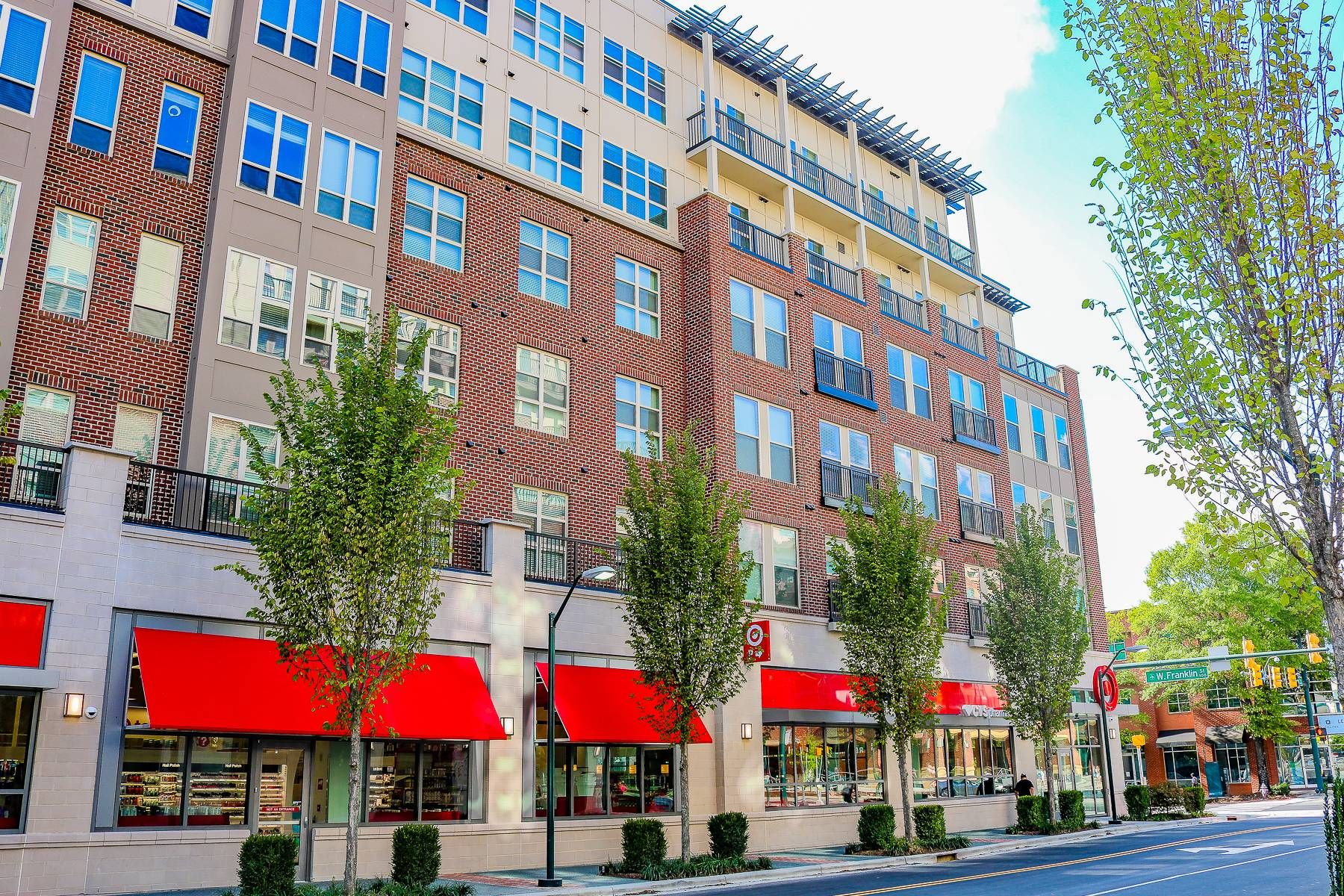 A modern apartment building with red awnings over ground-floor shops and trees lining the sidewalk.