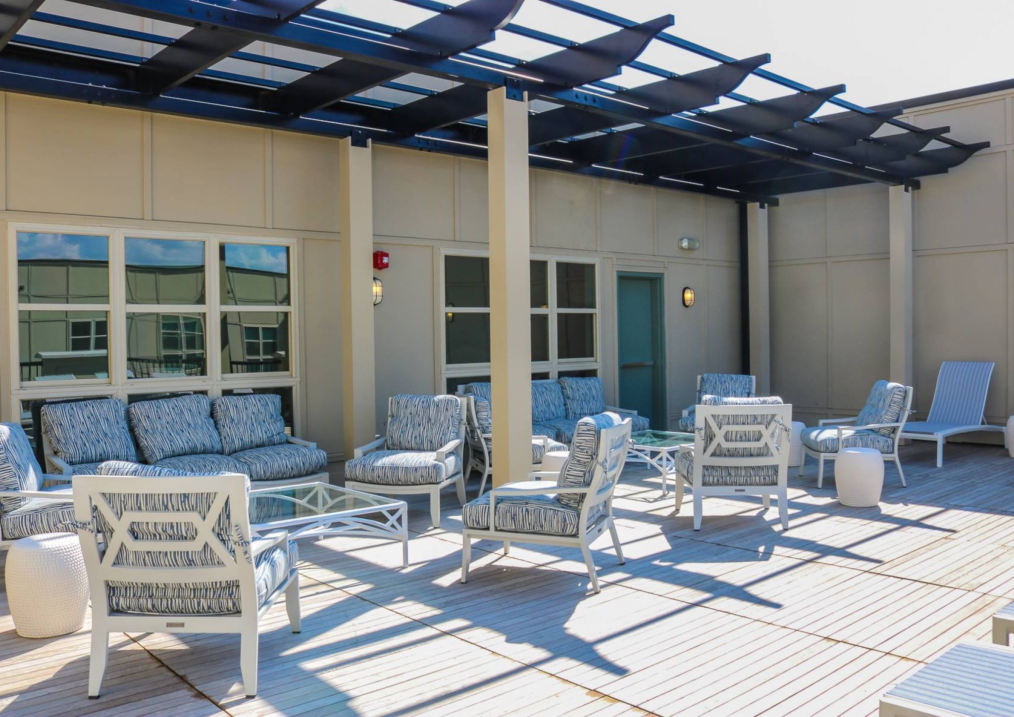 Outdoor patio with cushioned chairs, sofas, and tables under a modern pergola on a sunny day.