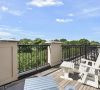 Rooftop deck with wooden chairs and railing overlooking green trees under a blue sky with clouds.