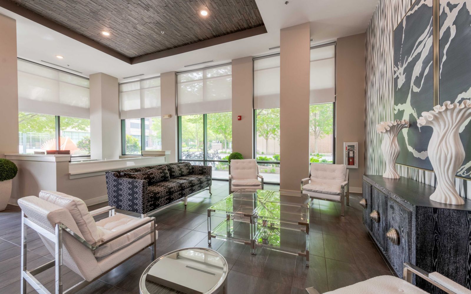 Modern lobby with large windows, stylish seating, glass tables, and decorative wall art and sculptures.